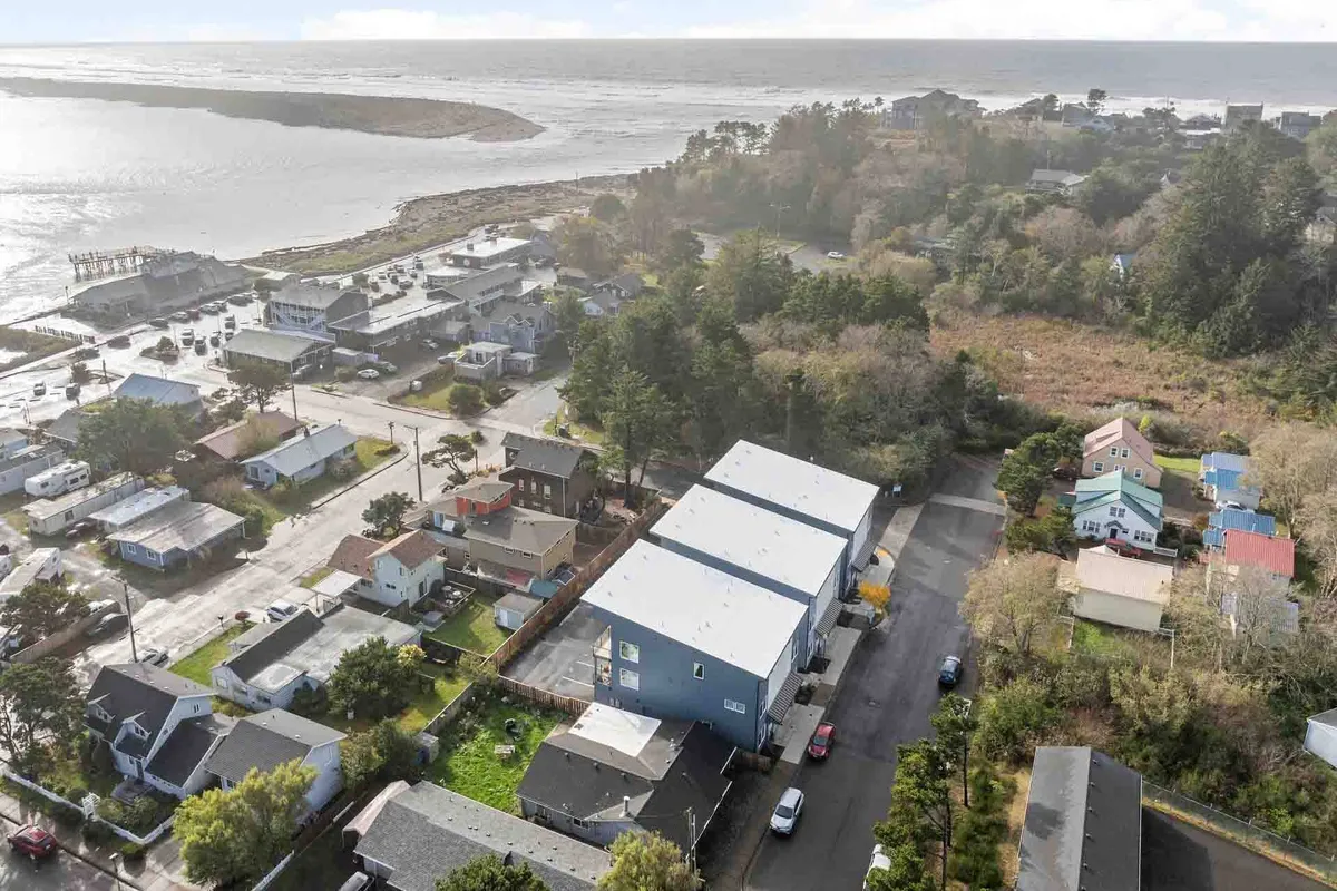 A wide ocean view with residential homes and a tree line, presenting a welcoming streetscape close to local attractions. The relaxed setting evokes a neighborhood where beach walks and community events are part of daily life, subtly suggesting nearby shops and eateries.