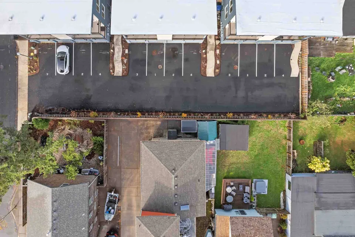 An exterior scene featuring a parking lot adjacent to residential houses and a lush green garden. The space hints at a welcoming community, with opportunities for gatherings or simply enjoying the outdoors.
