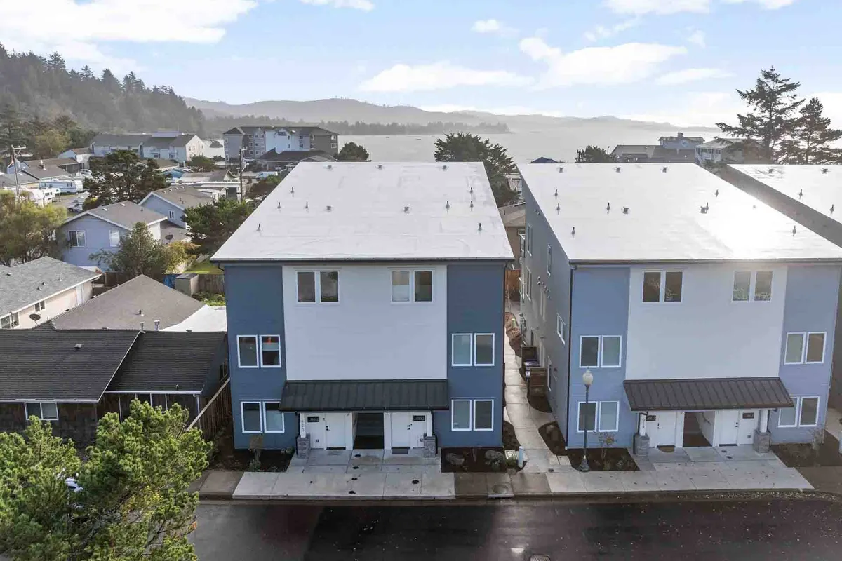 This image portrays a row of modern townhouses along a well-maintained street, framed by lush nearby greenery. The scene is bright and inviting, with the suggestion of neighbors enjoying outdoor activities such as walking or biking along the sidewalk.