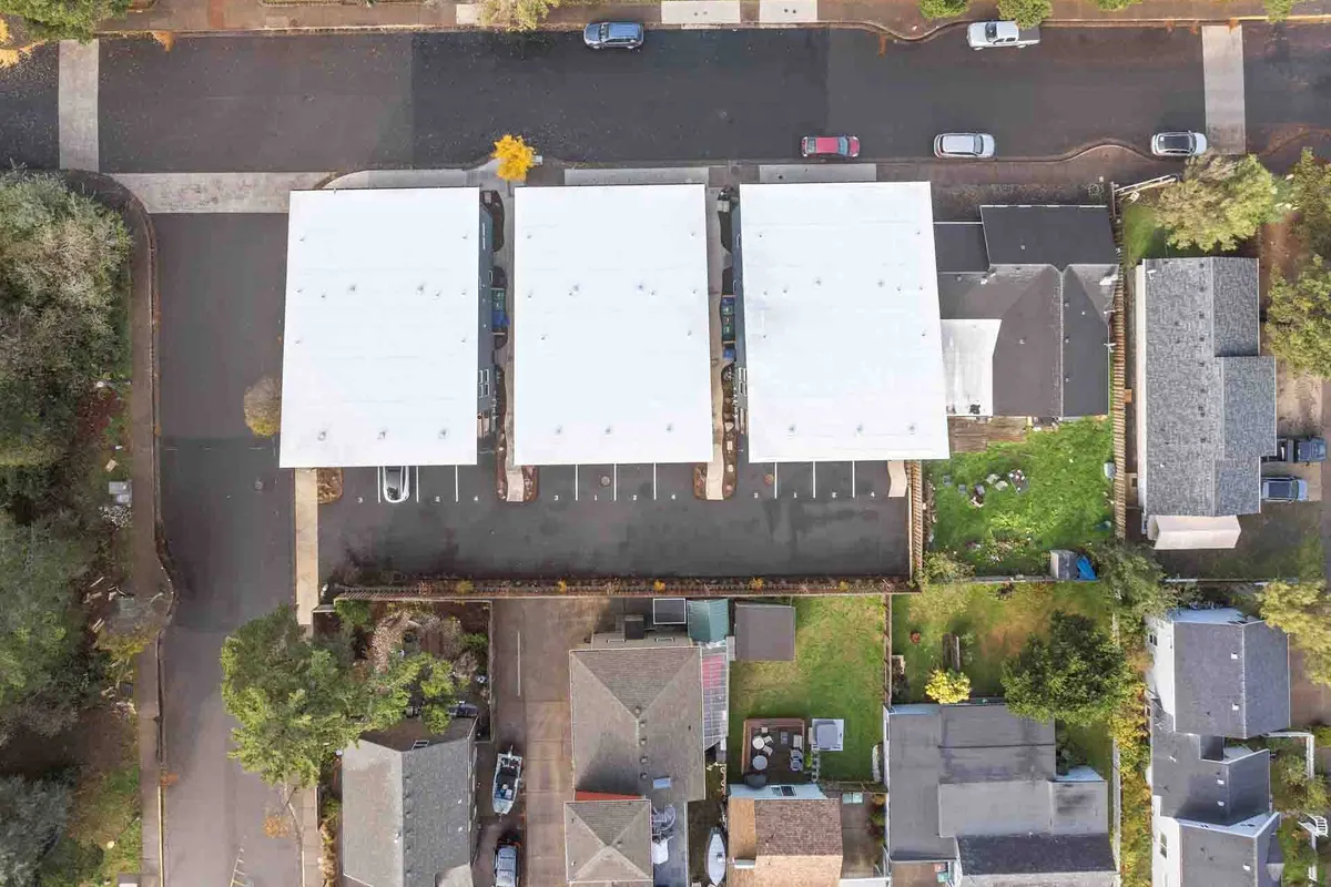 A bird’s-eye view of residential rooftops, a paved parking area, and surrounding homes. The setting is calm and organized, hinting at a peaceful residential environment where families gather, children play, and community celebrations might take place.