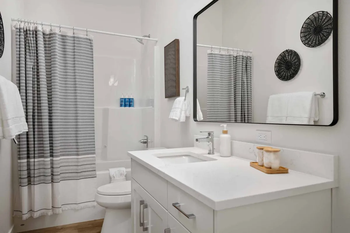 A refreshing and inviting en-suite bathroom with a modern vanity, sink, large mirror, shower area, and neatly folded bath towels. The space exudes a spa-like calm, ideal for self-care routines and relaxation.