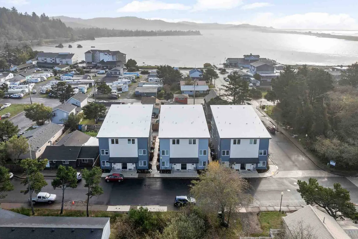 This exterior image features three modern houses overlooking the ocean, nestled in a vibrant neighborhood. The scene highlights the proximity to the water, showcasing a relaxed, social atmosphere and capturing the essence of community gatherings and local exploration.