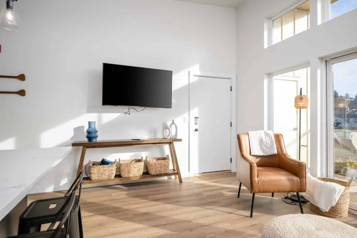 This interior shot focuses on a cozy corner with an armchair, wooden table, baskets, TV, and large windows that allow for plenty of natural light. The setup exudes a contemporary yet comfortable atmosphere, ideal for unwinding with pets after a day out.