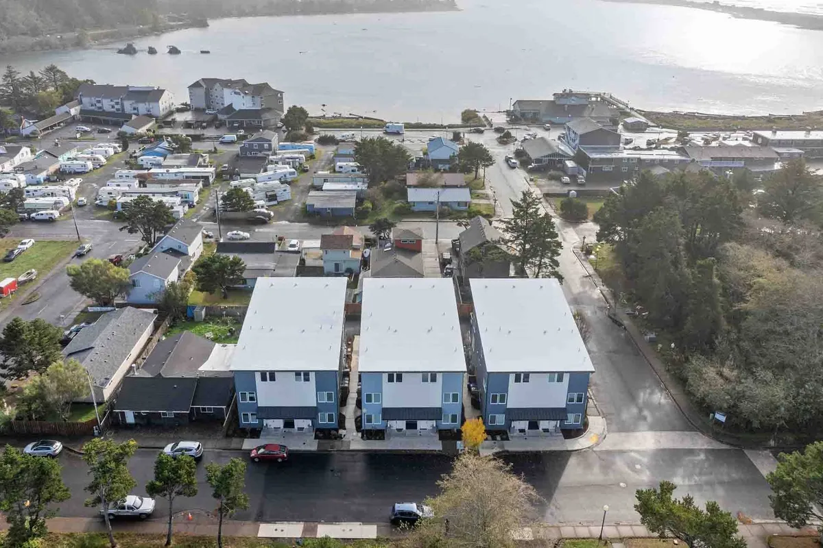 A wide exterior view showcasing three modern townhouses surrounded by green spaces and a nearby water body. The inviting lawn and peaceful setting suggest ample outdoor space and community ambiance.